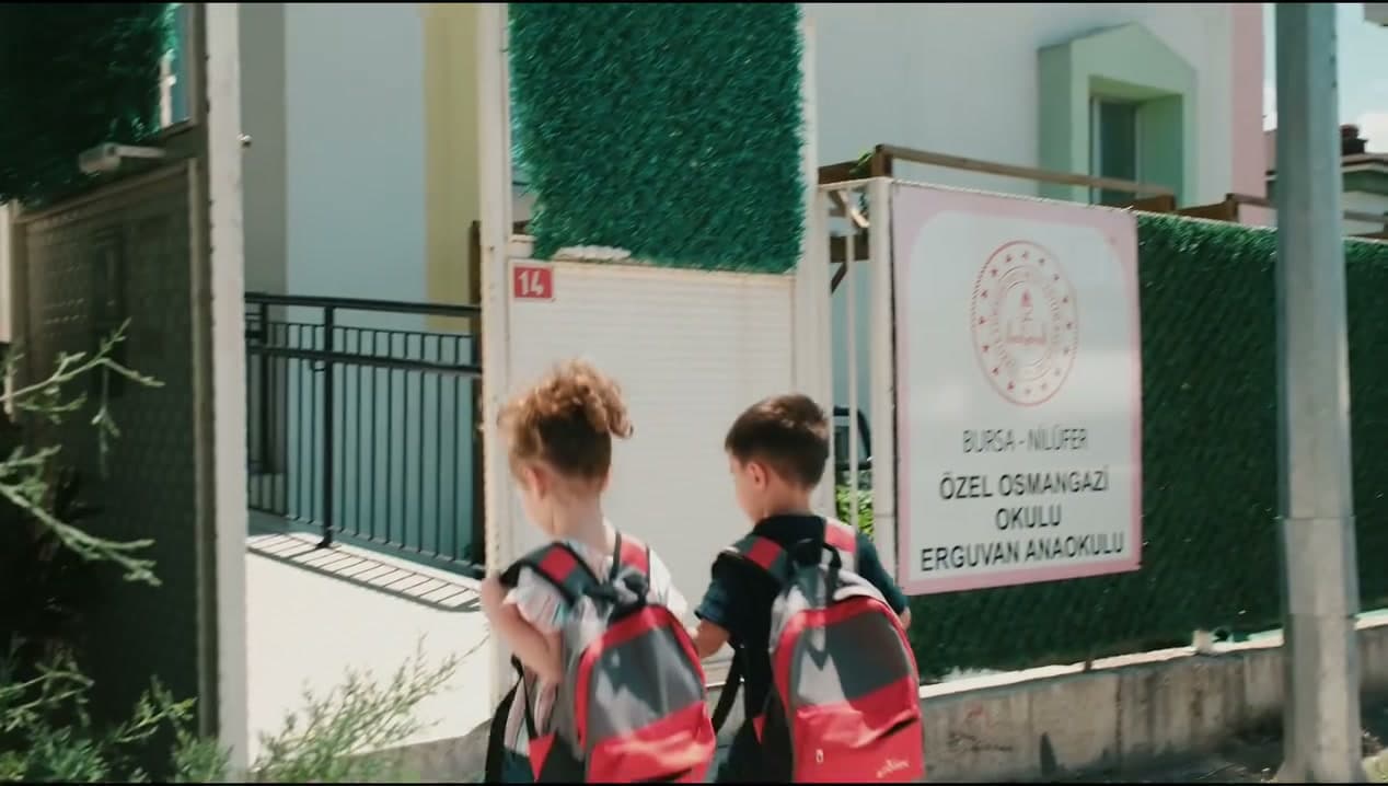 Sırt çantalı iki çocuk Özel Osmangazi Okulu Erguvan Anaokulu tabelasının önünden okula giriyor