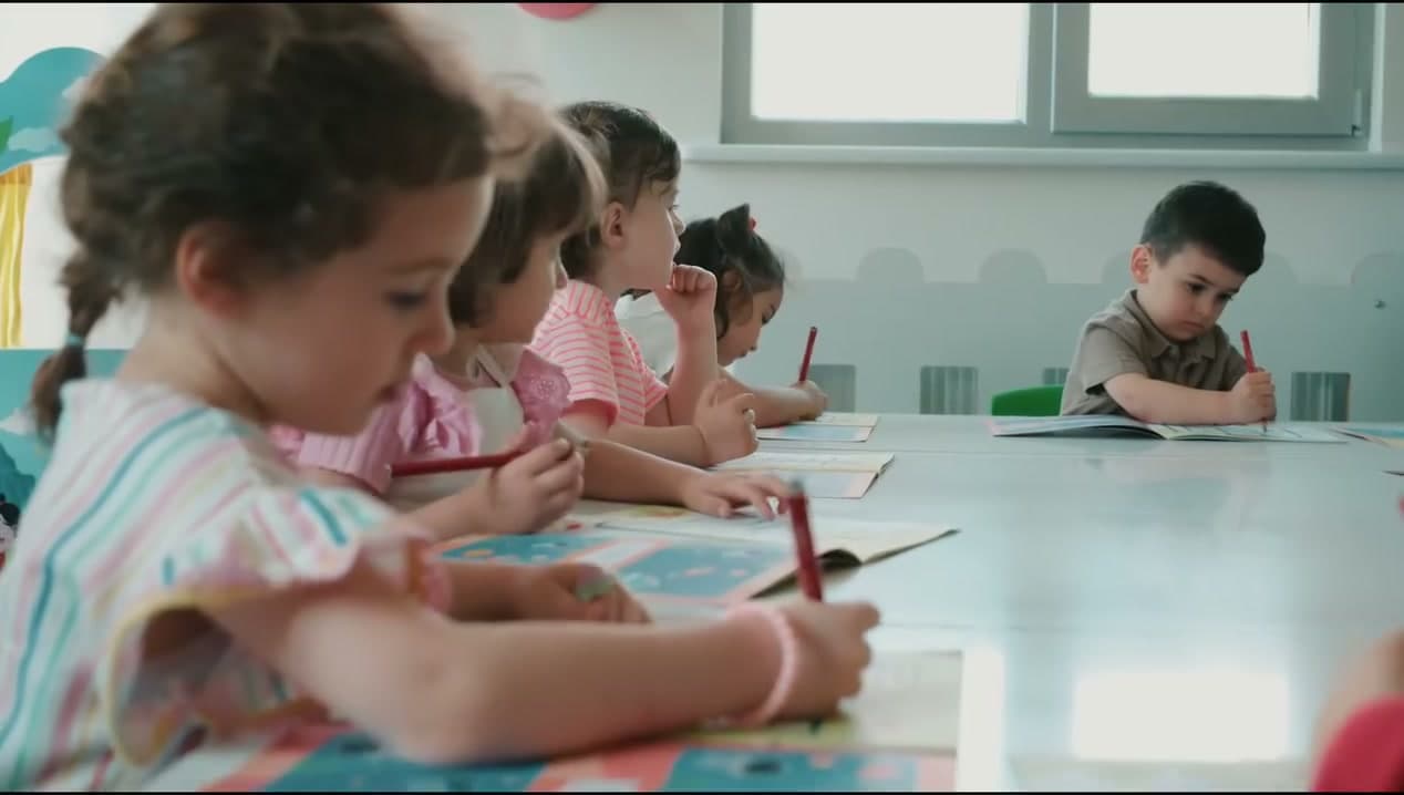 Uzun masada boyama ve yazı çalışması yapan çocuklar